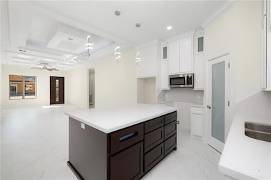 Kitchen with white cabinets, a center island, decorative light fixtures, stainless steel microwave, and open floor plan
