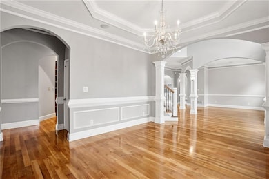 Spare room featuring light wood-style flooring, a tray ceiling, crown molding, arched walkways, and a chandelier