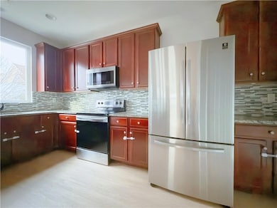 Kitchen featuring appliances with stainless steel finishes, tasteful backsplash, light stone counters, and reddish brown cabinets