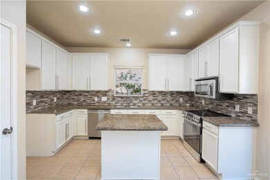 Kitchen featuring stainless steel appliances, a kitchen island, light tile patterned flooring, dark stone counters, and white cabinets