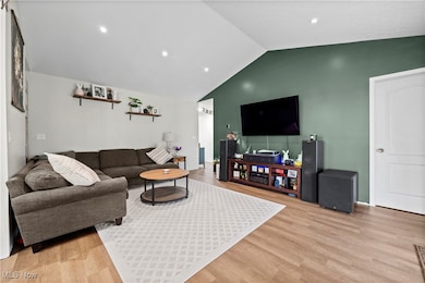 Living room with light wood finished floors, vaulted ceiling, and baseboards