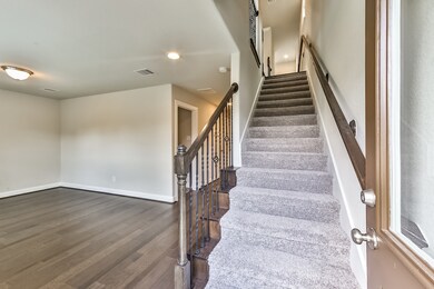 This photo showcases a modern interior with a staircase leading upstairs, featuring carpeted steps and a wooden handrail. The adjacent room has hardwood flooring, neutral walls, and a ceiling light, creating a bright and inviting space.