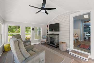 Living area featuring wood finished floors, lofted ceiling, a glass covered fireplace, a ceiling fan, and wooden walls