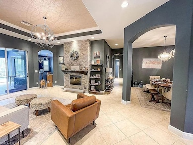 Living area with a raised ceiling, a chandelier, arched walkways, a stone fireplace, and recessed lighting