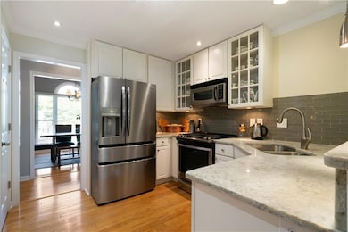 Kitchen with stainless steel appliances, light stone counters, crown molding, white cabinets, and tasteful backsplash