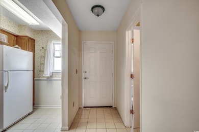 Kitchen with freestanding refrigerator, wallpapered walls, light tile patterned floors, brown cabinetry, and baseboards