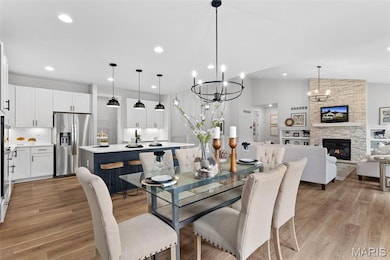 Dining area featuring light wood-type flooring, a stone fireplace, recessed lighting, lofted ceiling, and a chandelier