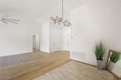 Unfurnished dining area with high vaulted ceiling, light wood-type flooring, arched walkways, a chandelier, and a ceiling fan