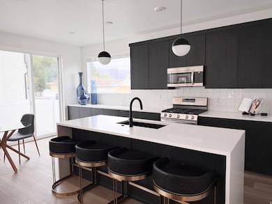 Kitchen featuring a kitchen breakfast bar, appliances with stainless steel finishes, an island with sink, pendant lighting, and light wood-style flooring