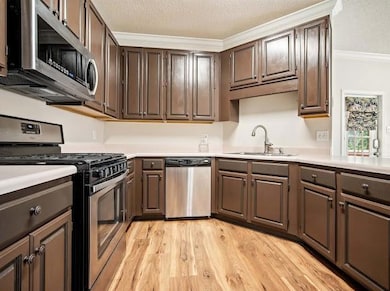 Kitchen featuring appliances with stainless steel finishes, ornamental molding, light countertops, light wood-style flooring, and a textured ceiling
