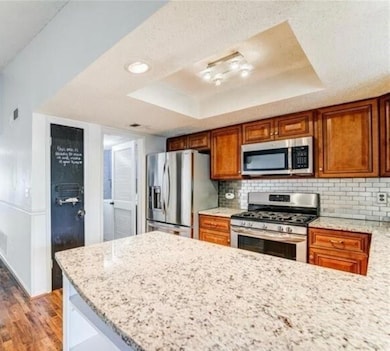 Kitchen featuring light stone counters, a raised ceiling, appliances with stainless steel finishes, a peninsula, and decorative backsplash