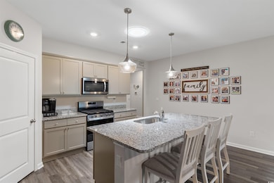 Kitchen with appliances with stainless steel finishes, dark wood finished floors, a breakfast bar area, light stone counters, and pendant lighting