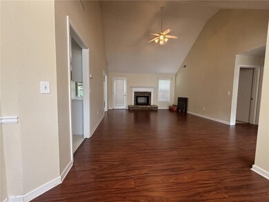 Unfurnished living room featuring ceiling fan, high vaulted ceiling, dark wood-type flooring, healthy amount of natural light, and a brick fireplace