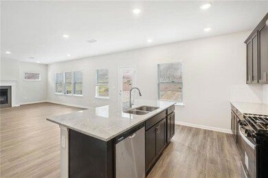 Kitchen with appliances with stainless steel finishes, light wood finished floors, an island with sink, light stone counters, and a glass covered fireplace