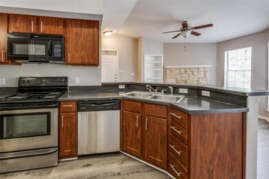 Kitchen with stainless steel appliances, a peninsula, light wood-style floors, ceiling fan, and dark countertops