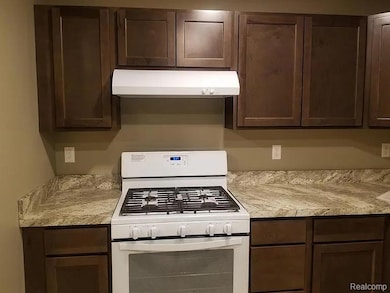 Kitchen with white gas range oven, dark brown cabinetry, and under cabinet range hood