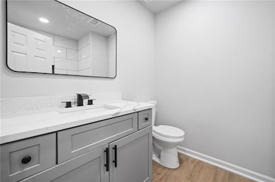 Bathroom featuring wood finished floors, vanity, toilet, and baseboards