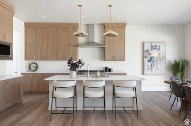 Kitchen featuring wood finished floors, wall chimney exhaust hood, a breakfast bar, recessed lighting, and decorative light fixtures