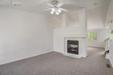 Unfurnished living room with carpet floors, a tiled fireplace, a ceiling fan, and high vaulted ceiling