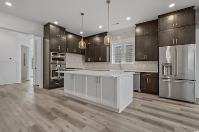 Kitchen featuring appliances with stainless steel finishes, hanging light fixtures, dark brown cabinetry, white cabinets, and recessed lighting