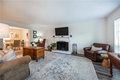 Living area featuring a chandelier, crown molding, wood finished floors, and a fireplace with raised hearth