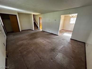 Empty room with a textured ceiling, a chandelier, stairway, and carpet floors
