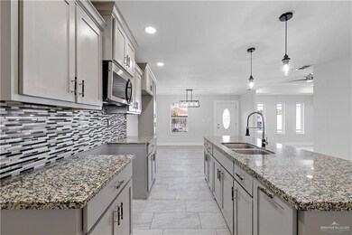 Kitchen with decorative backsplash, decorative light fixtures, a kitchen island with sink, light stone counters, and sink
