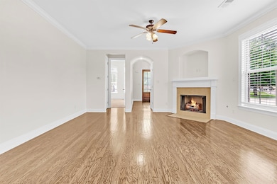 Unfurnished living room featuring a fireplace, wood finished floors, crown molding, plenty of natural light, and a ceiling fan