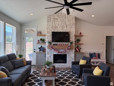 Living area featuring vaulted ceiling, a fireplace, ceiling fan, wood finished floors, and recessed lighting
