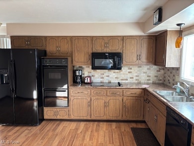 Kitchen featuring black appliances, tasteful backsplash, light wood-style floors, and brown cabinets