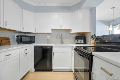 Kitchen with black appliances, white cabinets, crown molding, and backsplash