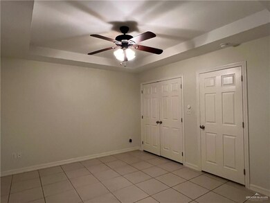Empty room with ceiling fan, a raised ceiling, and light tile patterned flooring