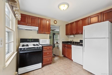 Kitchen with white appliances, under cabinet range hood, light tile patterned flooring, dark stone countertops, and a baseboard radiator