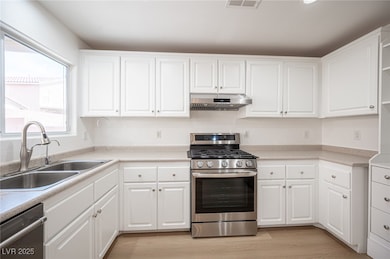 Kitchen with appliances with stainless steel finishes, white cabinetry, light countertops, light wood-style floors, and under cabinet range hood