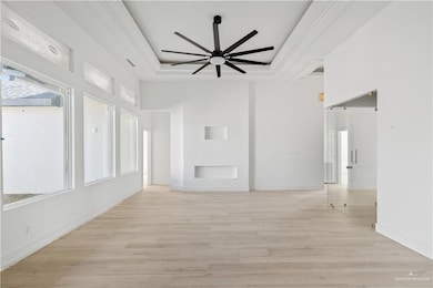 Unfurnished living room featuring light wood-type flooring, a raised ceiling, ceiling fan, and a towering ceiling