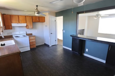 Kitchen featuring ceiling fan, white electric stove, under cabinet range hood, brown cabinets, and dark wood-type flooring