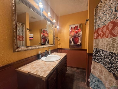 Bathroom featuring a textured ceiling, vanity, a textured wall, and stone finish floors