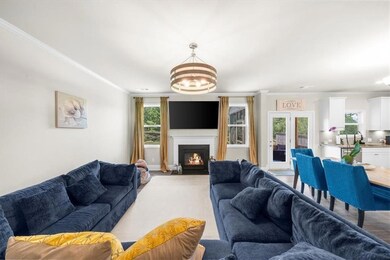 Living area featuring a chandelier, crown molding, a lit fireplace, and light carpet