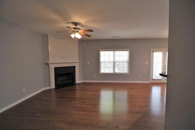Unfurnished living room with dark wood-style floors, a fireplace with flush hearth, and a ceiling fan