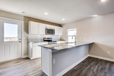 Kitchen featuring sink, appliances with stainless steel finishes, white cabinetry, light stone counters, and kitchen peninsula