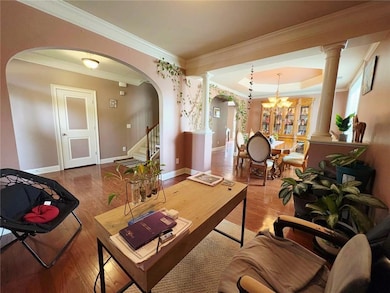 Living room featuring ornate columns, arched walkways, wood finished floors, a chandelier, and crown molding