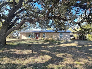 Ranch-style home featuring a carport, a metal roof, stone siding, covered front porch, mature trees, and a large front yard