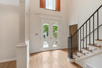 Grand 17x11 Entry Featuring Soaring 20-Foot Ceiling, Stunning Twisted Iron Staircase, Hardwood Floors, and Double Glass Doors with Transom Window and Plantation Shutters Above - A Truly Elegant First Impression!