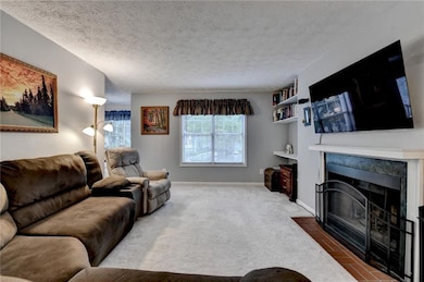 Carpeted living room with a tiled fireplace, a textured ceiling, baseboards, and built in features