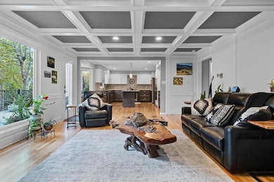 Living room with light wood-type flooring, beamed ceiling, coffered ceiling, ornamental molding, and a decorative wall