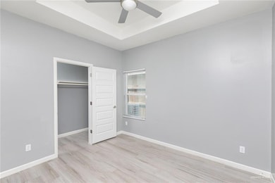 Unfurnished bedroom featuring light wood-style flooring, a tray ceiling, a closet, and a ceiling fan