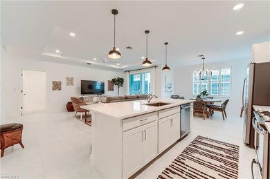 Kitchen with stainless steel appliances, a sink, a tray ceiling, light countertops, and an island with sink
