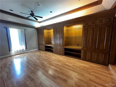 Unfurnished bedroom featuring a raised ceiling, light wood-style flooring, ceiling fan, and a textured ceiling