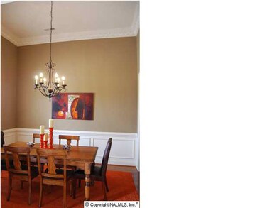 To the left is the dining room, chair rail shadow boxing and pendant light. Crown has detail that is reflected in the tops of columns. Wood floors.