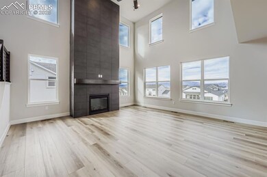 Unfurnished living room featuring a large fireplace, a towering ceiling, light wood-type flooring, and a ceiling fan